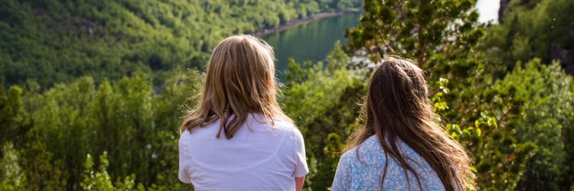 Two women sit overlooking a lush mountain landscape in Troms og Finnmark, Norway, on a sunny day.