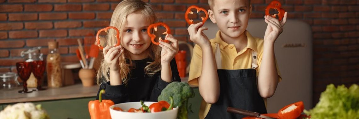 Two children holding capsicum slices while preparing vegetables in a cozy kitchen setting.